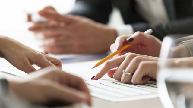 Projektbegleitung Eine Frauenhand zeigt auf ein Dokument und hält einen Stift in der Hand.